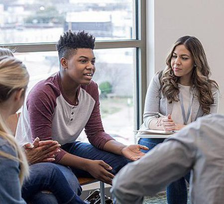 A group of younger people are sitting in chairs arranged in a circle. They are dressed casually, and discussing issues.