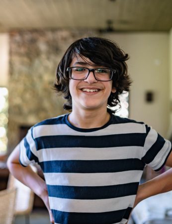 A teenage boy with mid length, dark-brown hair and large, dark-brown glasses is smiling for the picture.