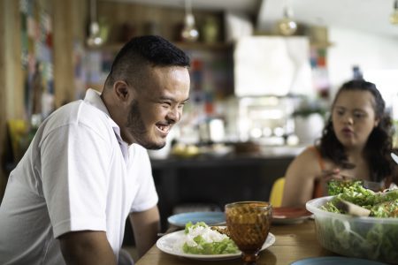A man and a woman sitting at a table with salads and drinks, smiling and conversing in a casual dining setting.